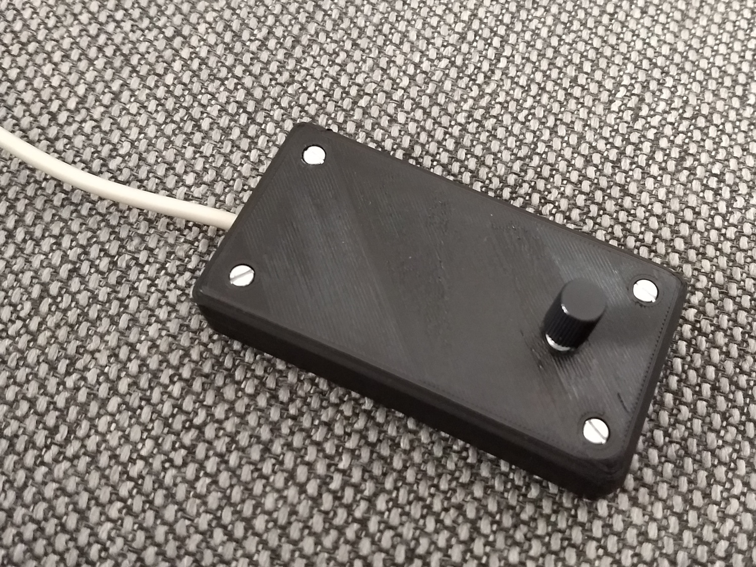 A black 3D printed case with a knob the top and a cable coming out of the side